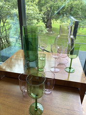 Gläser und Vasen aus Glas in Rosa und Grün auf einem Holztisch