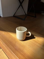 Tasse steht auf Holzboden mit Schatten und Sonnenlicht drumherum
