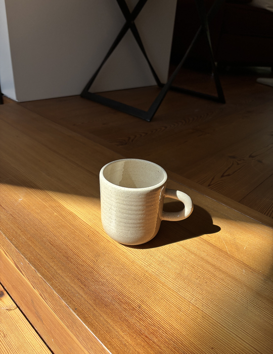 Tasse steht auf Holzboden mit Schatten und Sonnenlicht drumherum